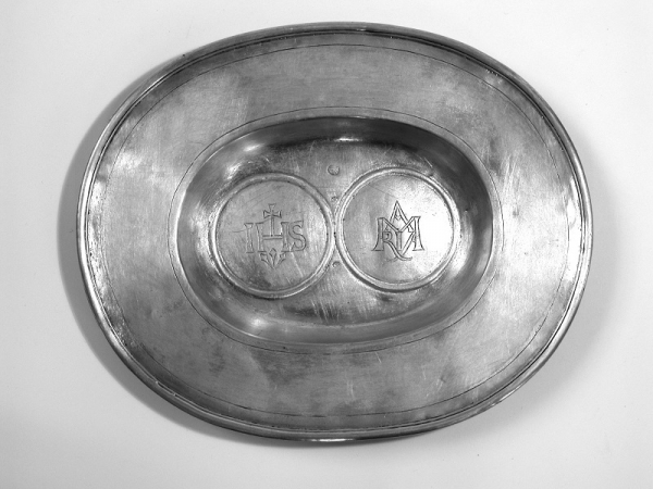 Tacka owalna, gładka, z szeroką kryzą i ostrym wrębem. W lustrze dwa kręgi w profilowanym obramieniu wewnątrz których grawerowane hagiogramy ''IHS'' i''. MARYA''.  Znaki; 1] imienny- inicjały ''G.S.'' w owalu- nierozpoznany, 2] pruski znak kontrybucyjny z lat 1809- 1812 z orłem