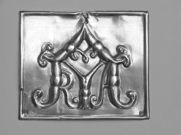 Plakieta prostokątna, obwiedziona na obrzeżu półwałkiem, z dużym stylizowanym hagiogramem ''MARYA''.